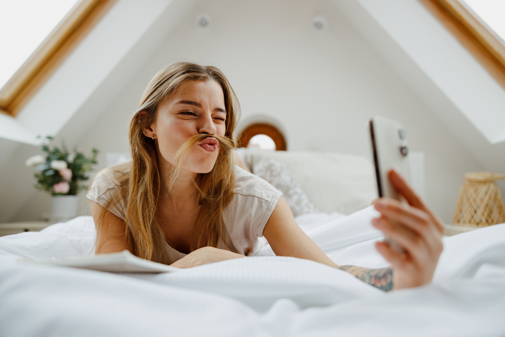 A woman on the bed, smiling, taking a selfie with her phone